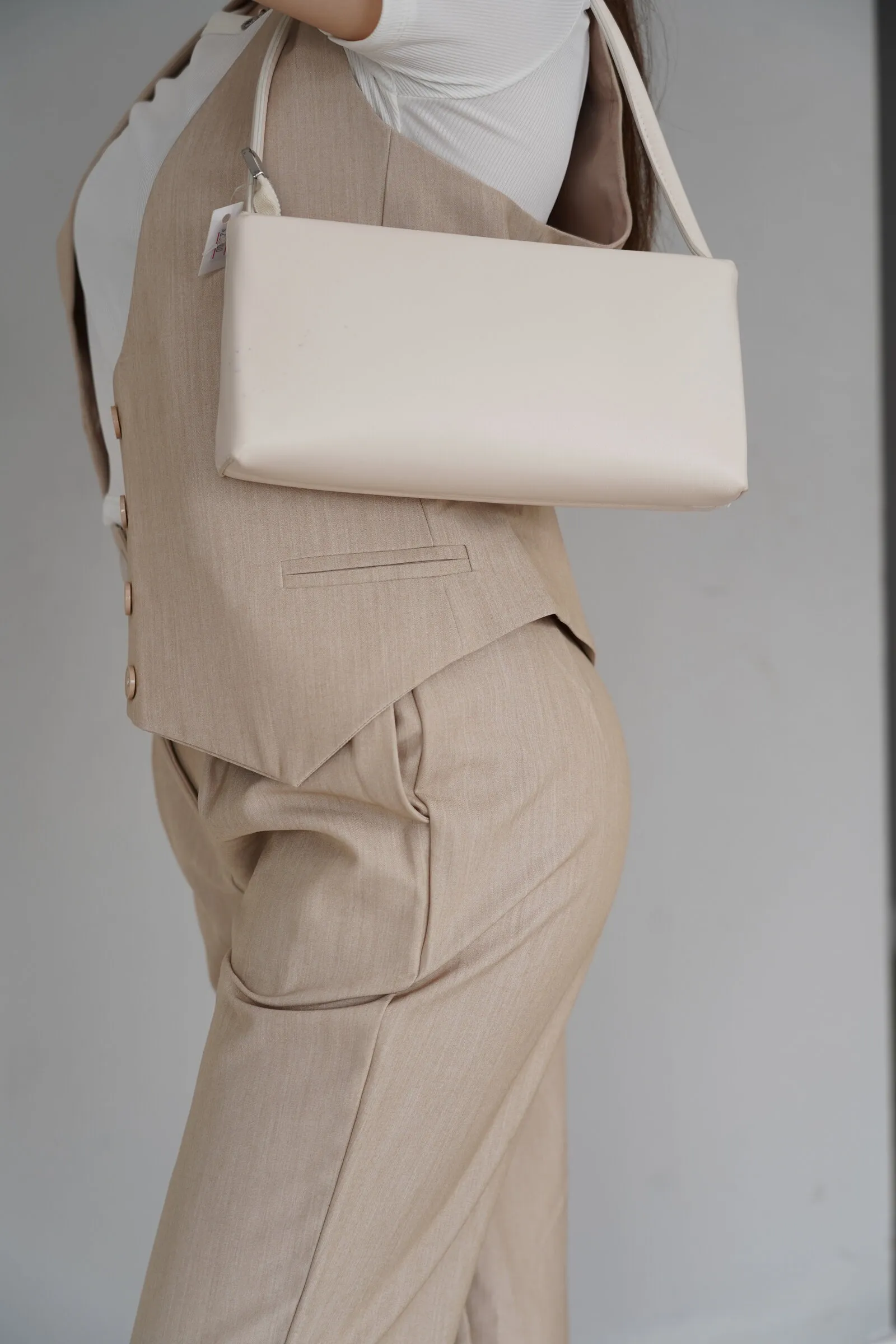 Detalle de conjunto de chaleco y pantalón beige con una cartera de cuero color crema al hombro.