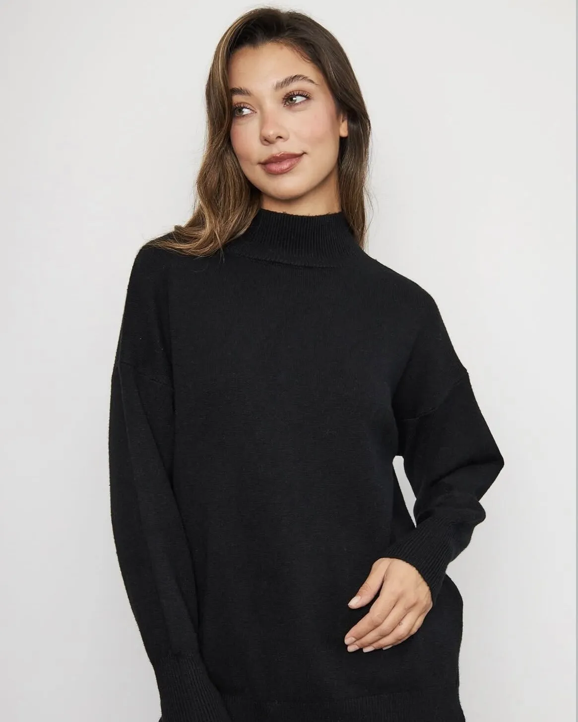 Modelo con sweater negro de cuello alto sobre fondo blanco de estudio.